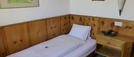 A single bed with a wooden headboard, a bedside table with a lamp, and two framed pictures on the wall.