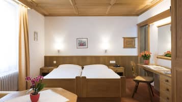 Una habitación de hotel con dos camas de madera, un escritorio con una silla, un aparador, un espejo y un ventanal con cortinas.