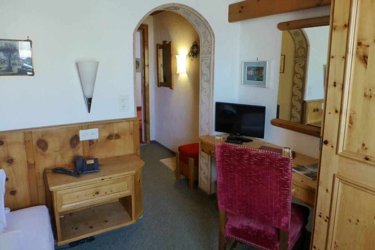 A room with a wooden desk, a chair, a television, and a mirror.