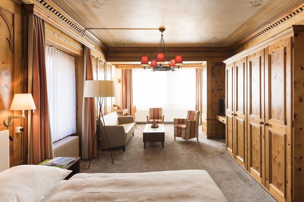 A hotel room with a large bed, a sofa, two armchairs, a coffee table, and a television.