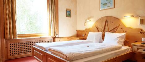 Una cama de madera con ropa de cama blanca, una ventana con cortinas, una lámpara de pared y un pequeño cuadro.