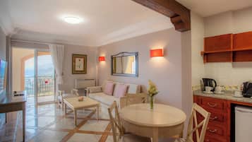 Una habitación bien iluminada con una mesa de comedor, sillas, un sofá, una zona de cocina con armarios y vistas a través de un ventanal.