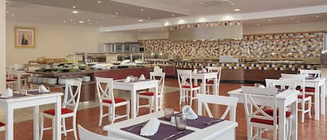 A restaurant with white tables and chairs, a buffet area, and a tiled backsplash.