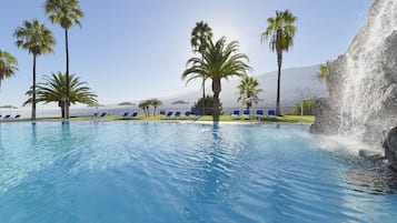 Una piscina con agua cristalina, rodeada de palmeras y sillas de descanso.