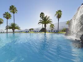 Una piscina con agua cristalina, rodeada de palmeras y sillas de descanso.