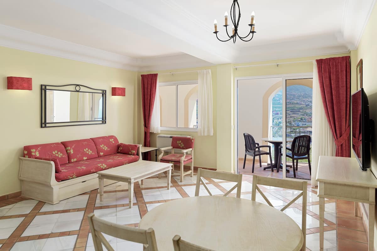 A living room with a sofa, coffee table, chairs, a TV, and a balcony with a view.