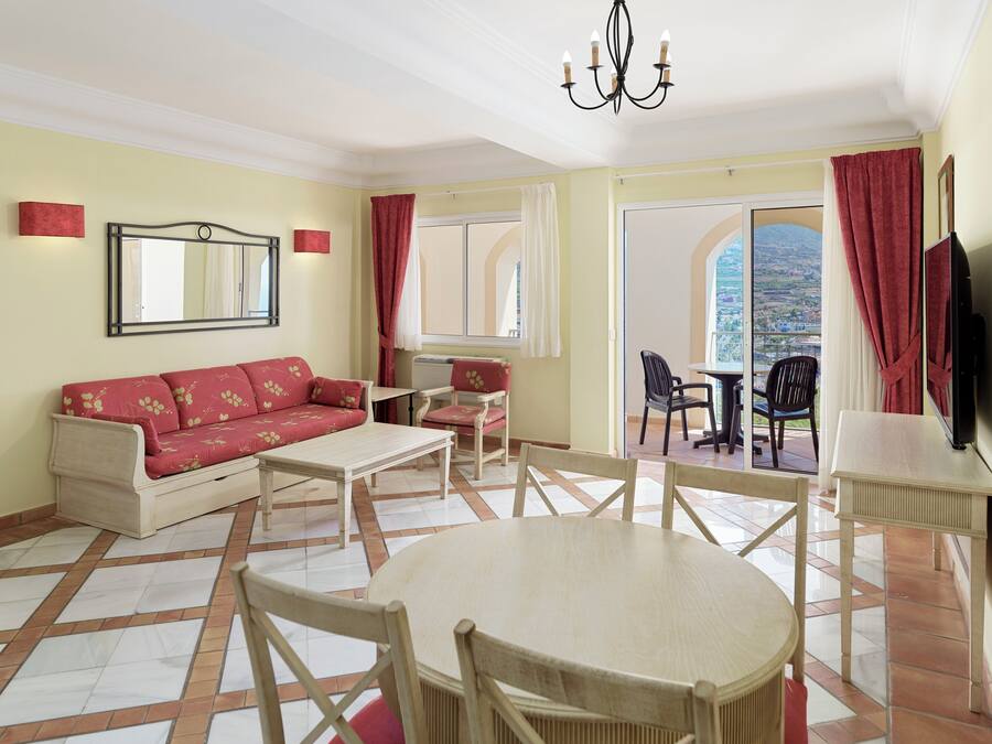 Una sala de estar con sofá, mesa de centro, sillas, televisor y balcón con vistas.