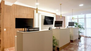 A hotel reception area with wooden paneling, a priority check-in sign, and two flat-screen TVs on the wall. - Hotel Las Aguilas Tenerife, Affiliated by Melia (Puerto de la Cruz)