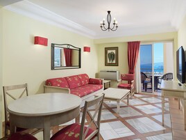 Una sala de estar con sofá, sillones, una mesa redonda, televisor y un balcón con vistas.