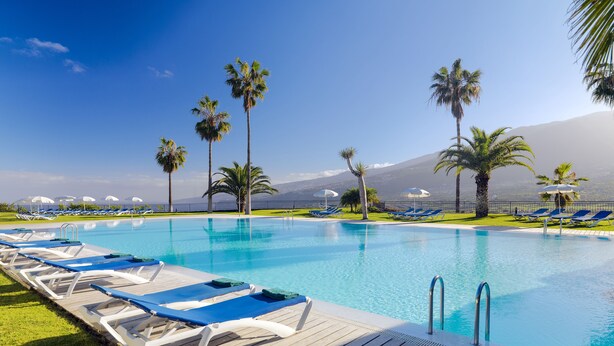 A pool area with lounge chairs and palm trees, surrounded by a fence and a mountain in the background. - Hotel Las Aguilas Tenerife, Affiliated by Melia (Puerto de la Cruz)
