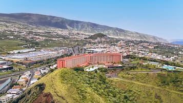A large red building with multiple floors, surrounded by a hilly landscape and a coastal view.