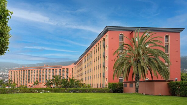 A large building with a red facade, multiple balconies, and a well-maintained lawn in front.