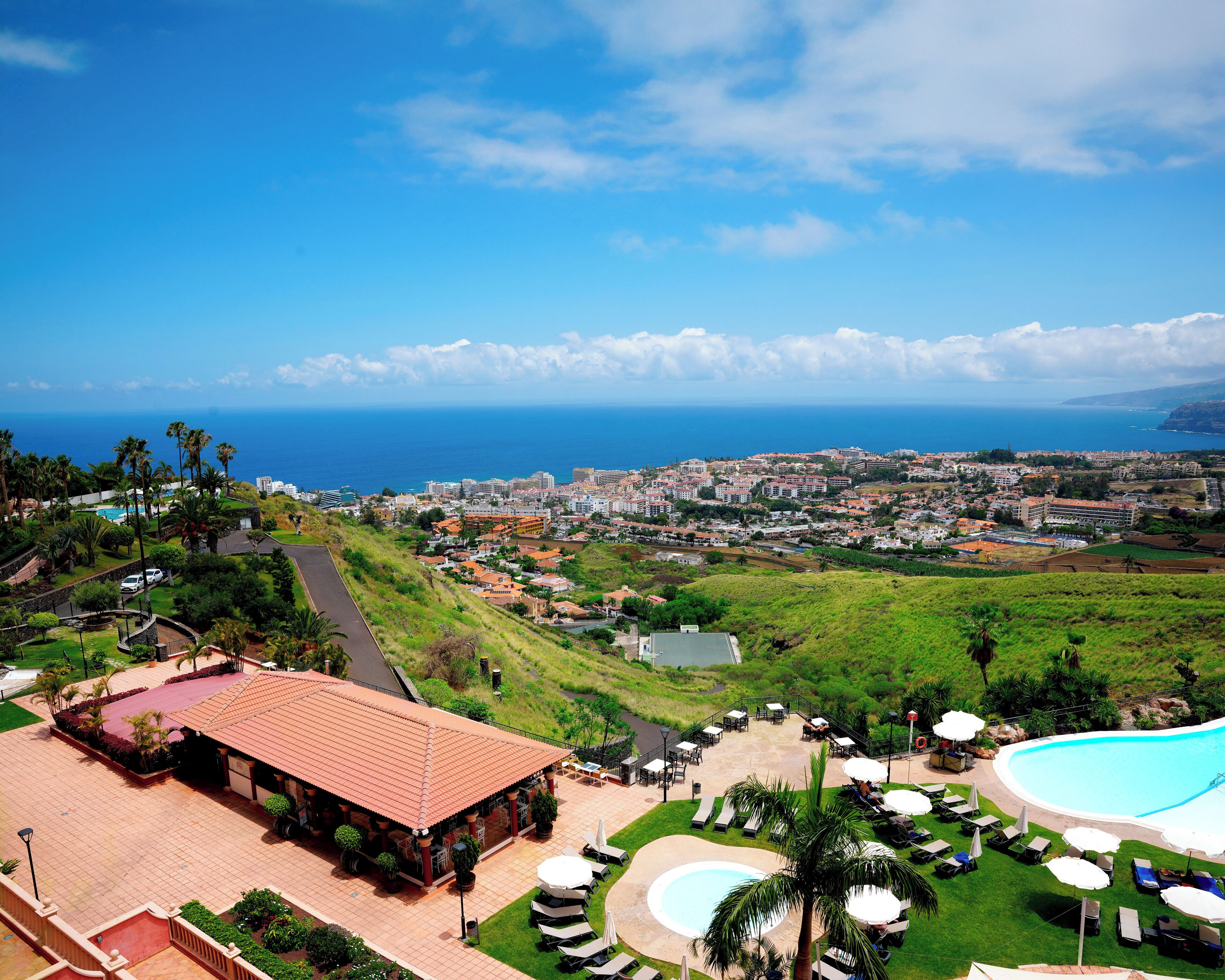 A resort with a swimming pool, outdoor seating, and a view of the ocean and cityscape.