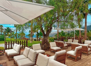 An outdoor seating area with wooden furniture and umbrellas, surrounded by lush greenery and a view of the sea. - Hotel Las Aguilas Tenerife, Affiliated by Melia (Puerto de la Cruz)