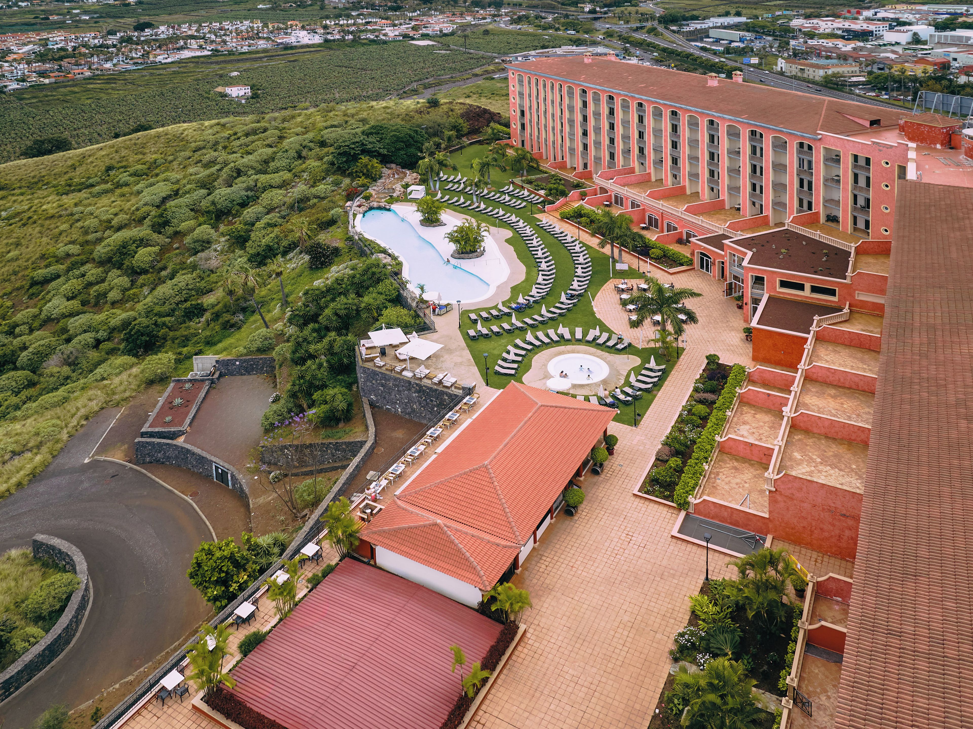 Un hotel con piscina, jardín ajardinado y un edificio grande con varios balcones.
