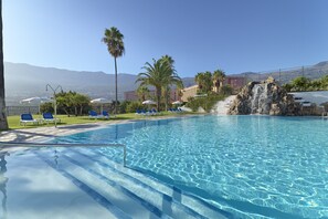 A clear swimming pool with blue water, surrounded by blue lounge chairs and umbrellas, with a view of mountains in the background. - Hotel Las Aguilas Tenerife, Affiliated by Melia (Puerto de la Cruz)