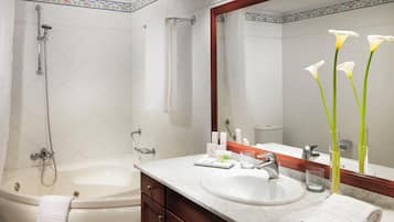 A bathroom with a bathtub, a sink, and a mirror. There are toiletries on the sink counter.