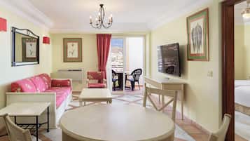 A room with a round table, a sofa, a TV, and a balcony with chairs.