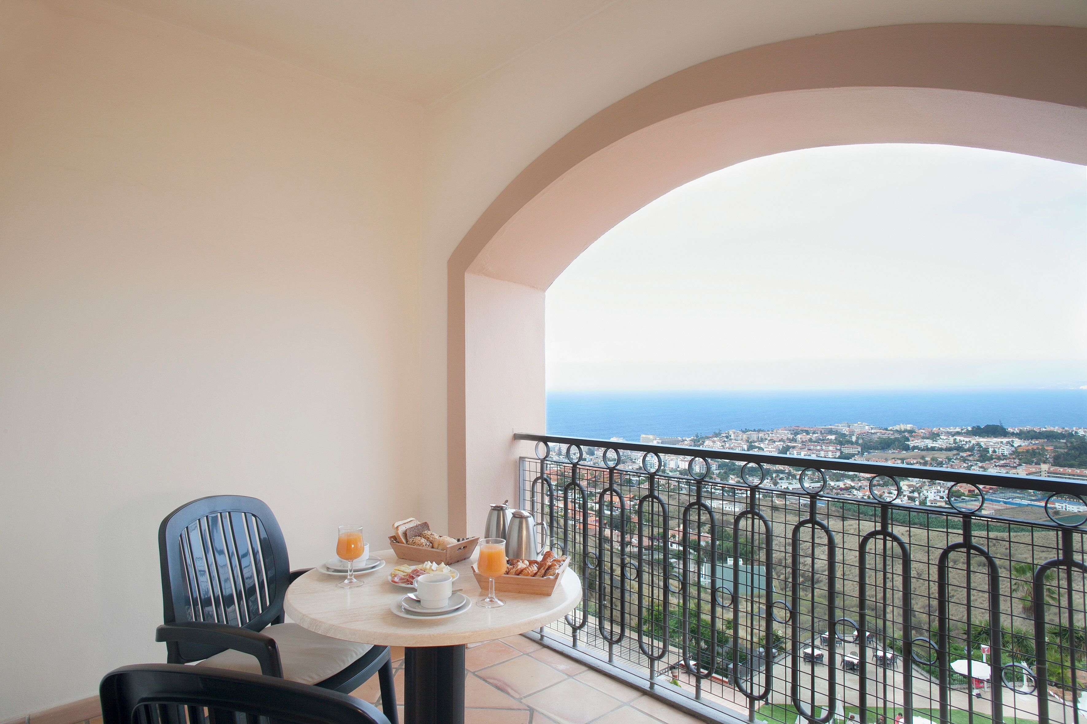 Een balkon met een ontbijtje, een stoel en uitzicht op de stad en zee.