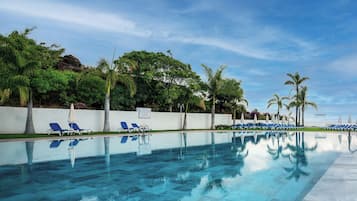 Piscina con agua azul cristalina, rodeada de palmeras y sillas de descanso.