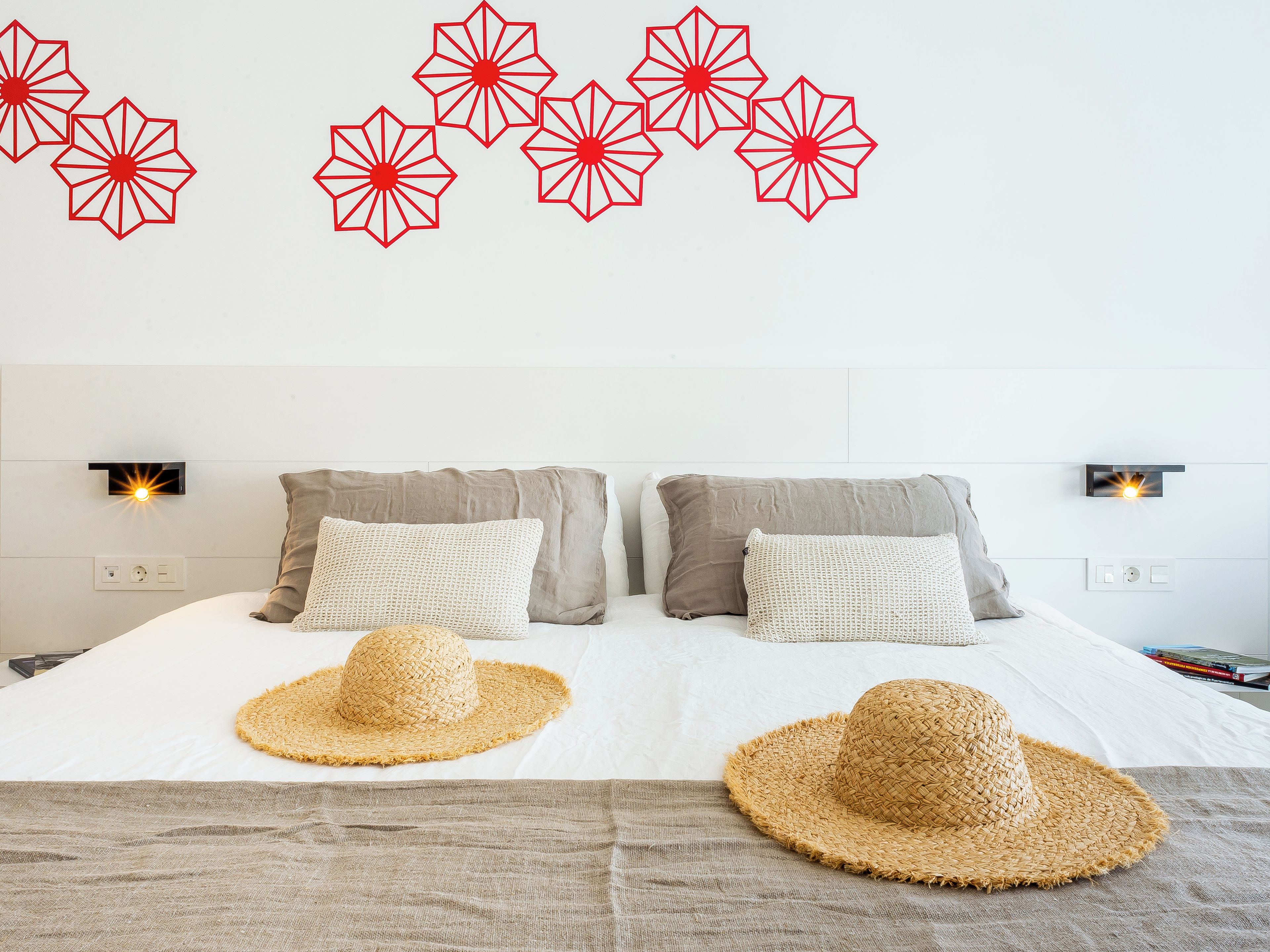 A bed with two pillows, a woven hat, and a wall with geometric wall art.