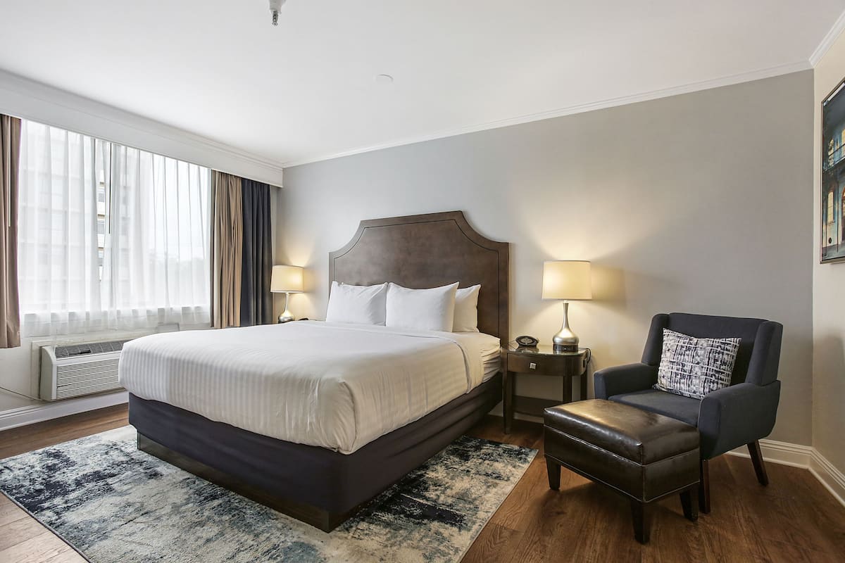 Une chambre d’hôtel avec un grand lit, des lampes de chevet, une chaise et une fenêtre avec des rideaux.