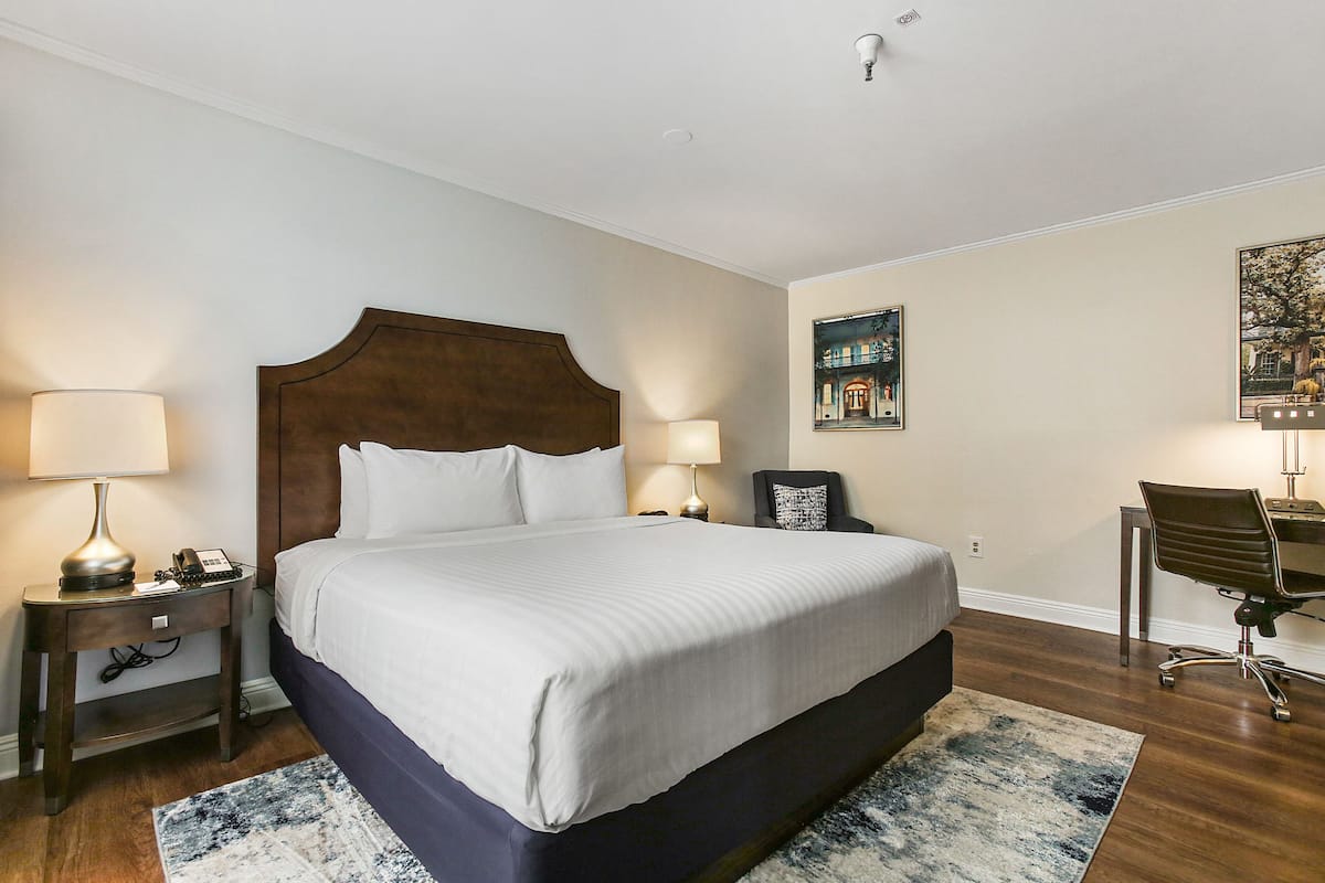 Une chambre bien rangée, avec un grand lit, deux tables de chevet avec des lampes, un bureau avec une chaise et un tableau accroché au mur.