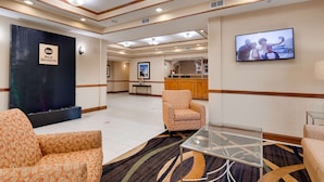 A hotel lobby with a reception desk, a TV screen, patterned sofas, and a glass coffee table.