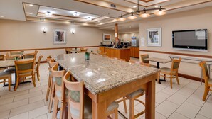 A spacious dining area with a large granite table surrounded by wooden chairs, a reception desk, and a flat-screen TV mounted on the wall.