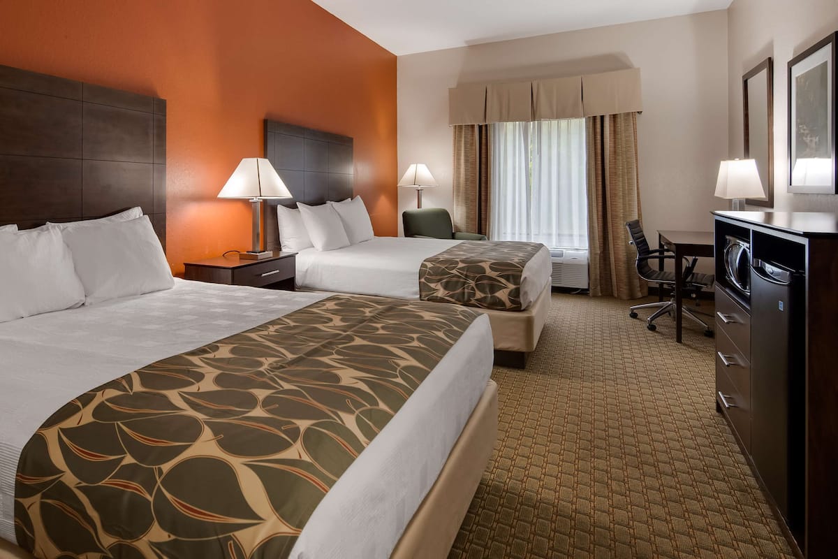 A hotel room with two beds, a desk, a chair, and a minibar.