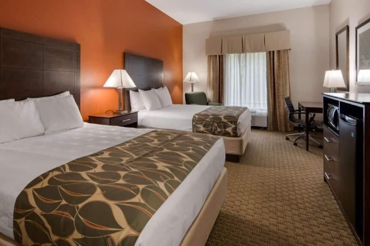A hotel room with two beds, a desk, a chair, a TV, and a wardrobe.