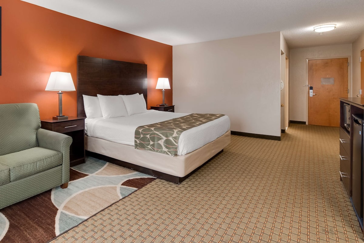 A hotel room with a bed, a green sofa, two bedside lamps, a wooden headboard, and a framed picture on the wall.