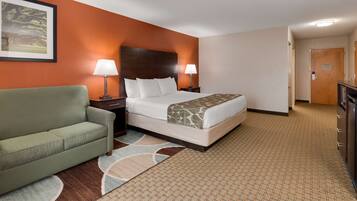 A hotel room with a bed, a green sofa, two bedside lamps, a wooden headboard, and a framed picture on the wall.