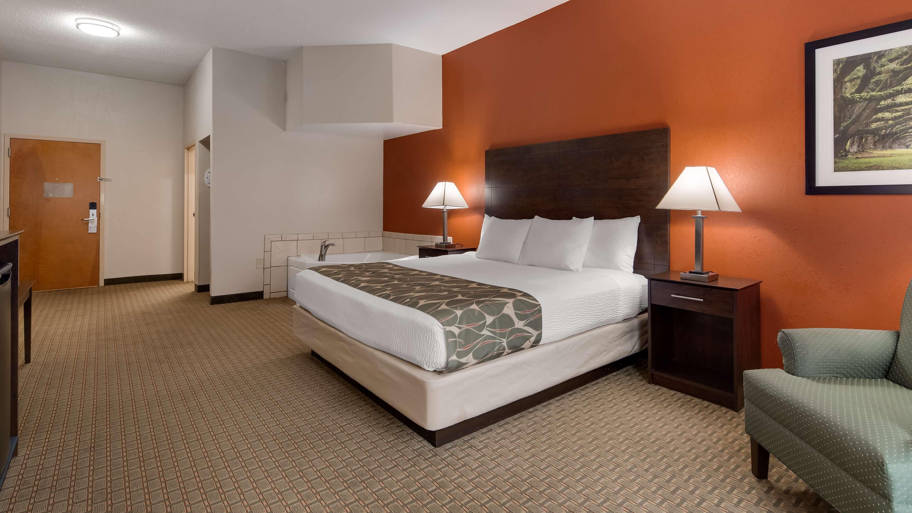 Una camera d'albergo con un letto grande, due lampade ai lati del letto, una testiera in legno, una poltrona verde e un quadro appeso al muro.