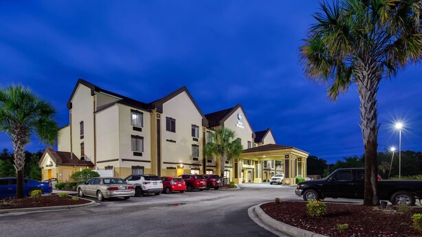 A hotel with a modern design, featuring a parking lot with several cars and a well-lit entrance.
