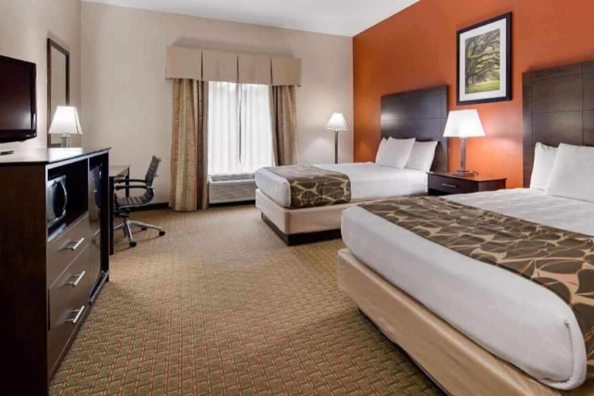 A hotel room with two beds, a desk with a chair, a TV, and a window with curtains.