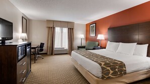 A hotel room with a bed, a desk with a chair, a television, a lamp, and a window with curtains.