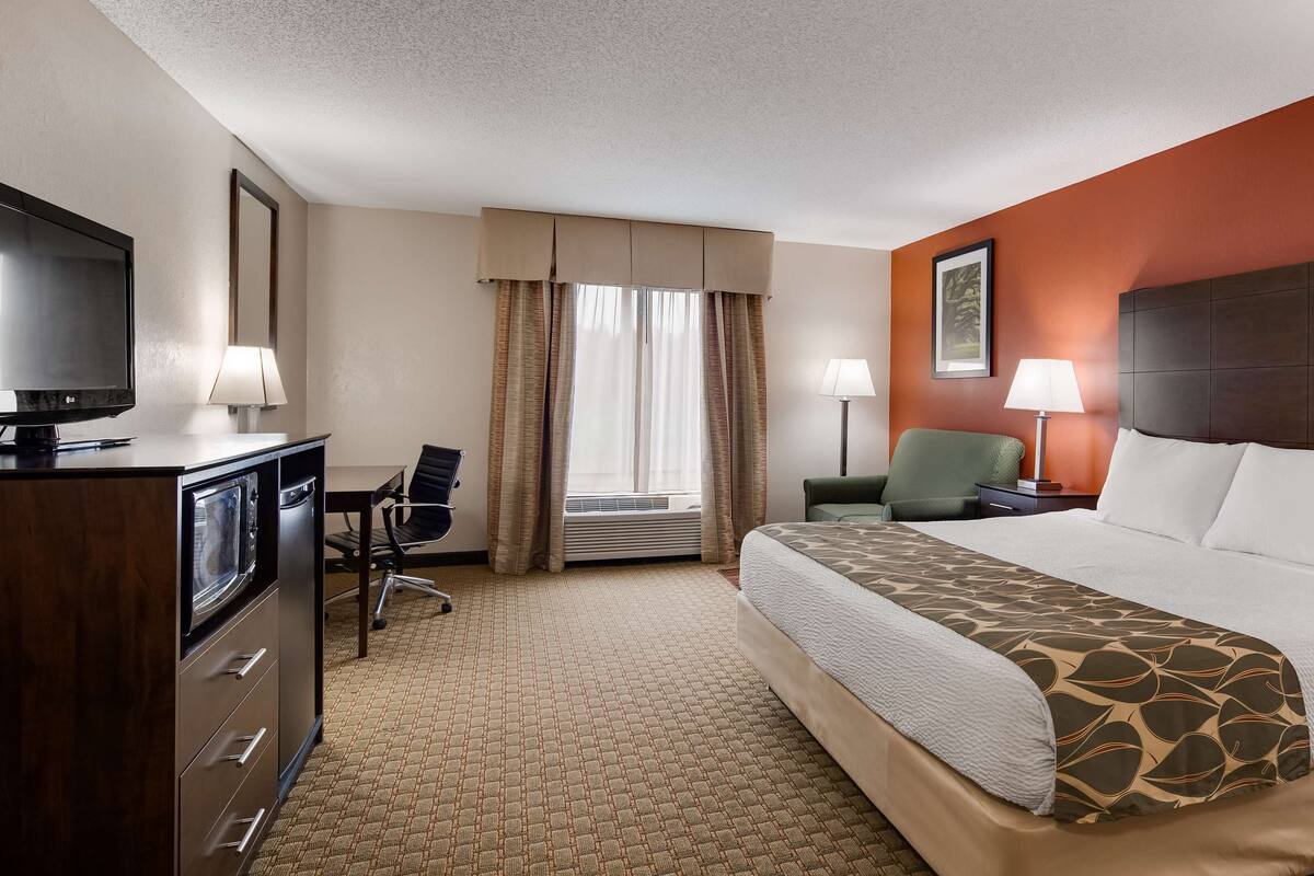 A hotel room with a bed, a desk with a chair, a television, a lamp, and a window with curtains.