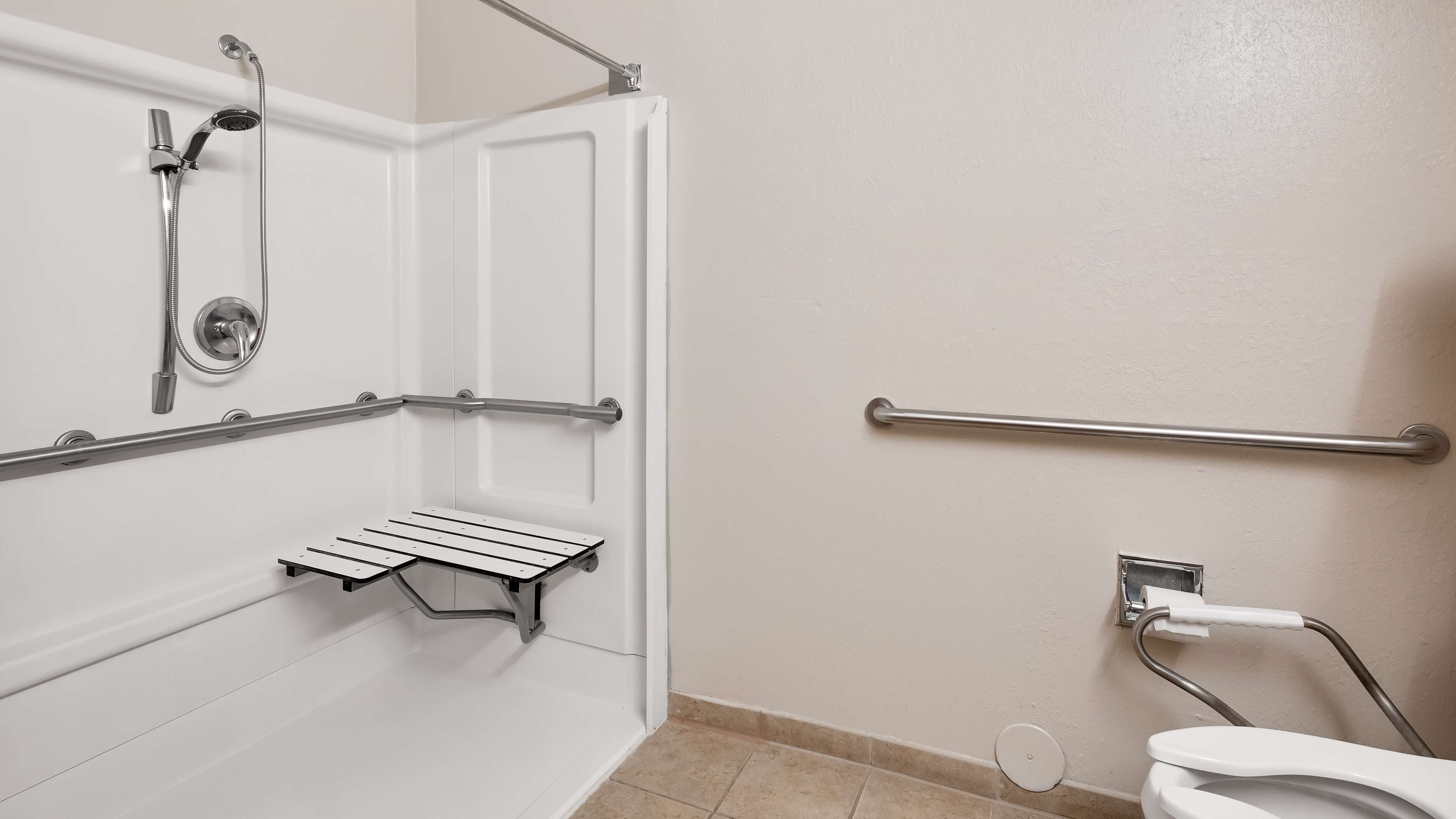 A bathroom with a shower, grab bars, a toilet, and a hand dryer.