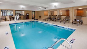 A hotel pool area with a clear blue pool, lounge chairs, and a reception desk.
