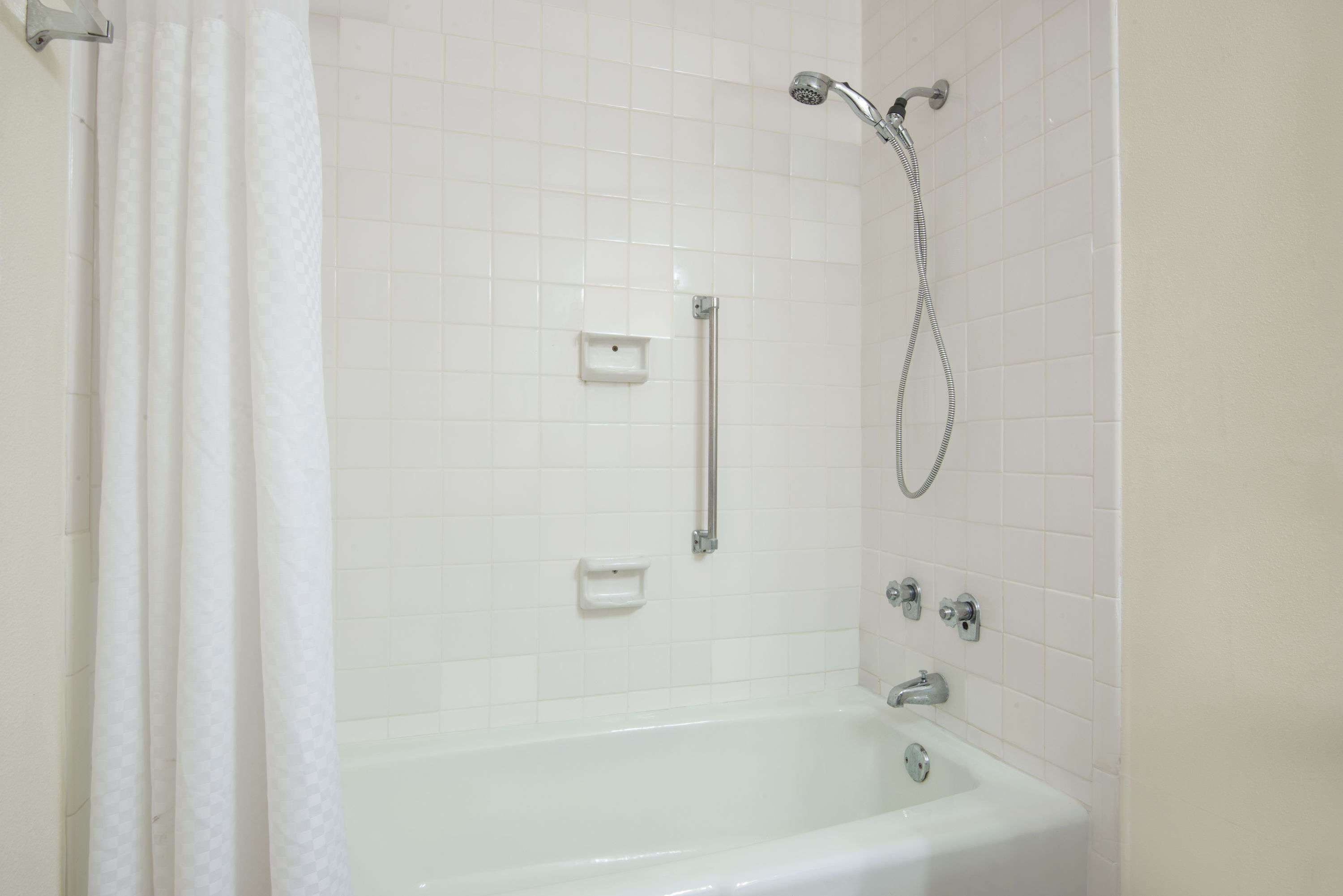 A bathroom with a white bathtub, a showerhead, and a handrail.