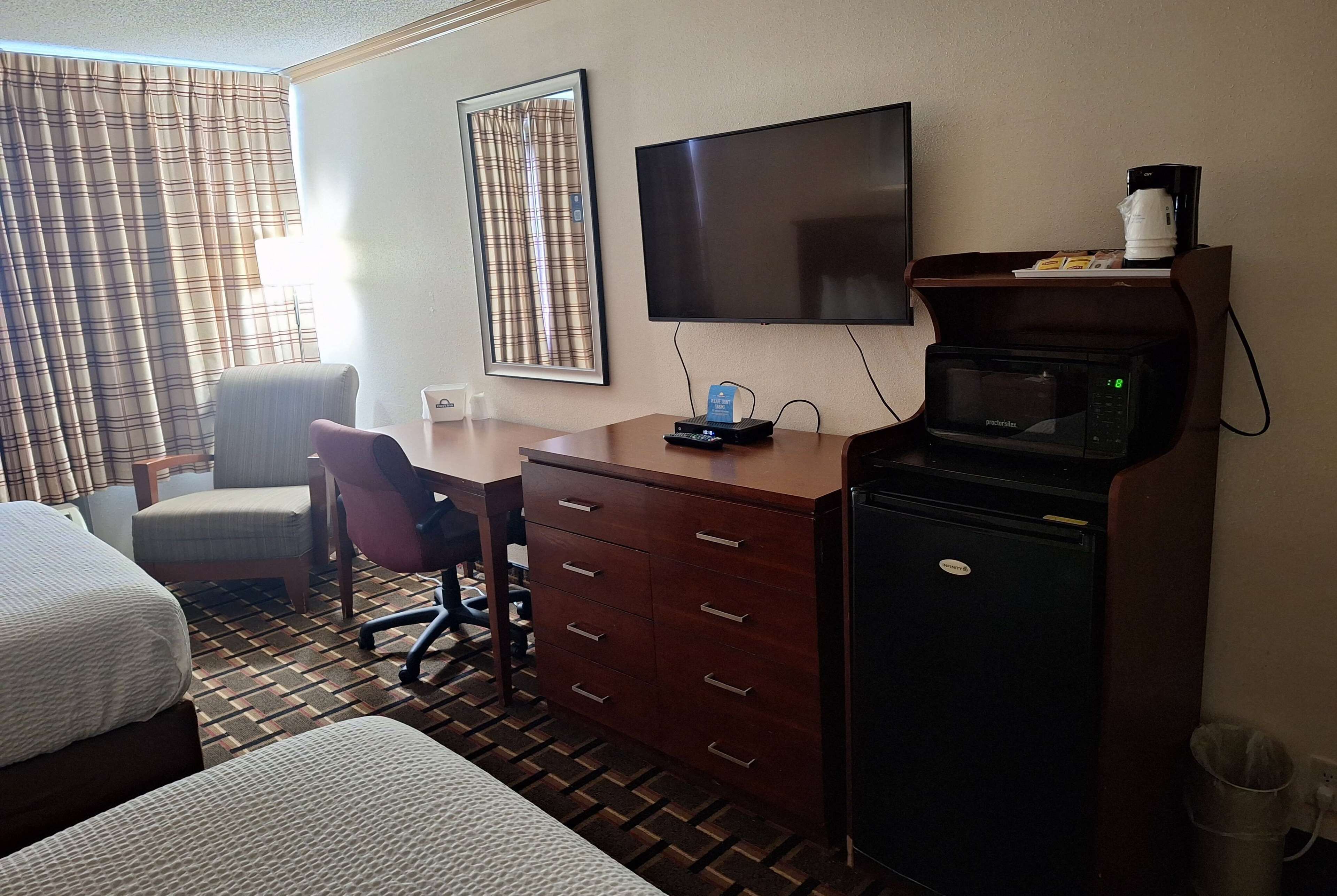 A hotel room with two beds, a desk with a chair, a television, a microwave, and a coffee maker.