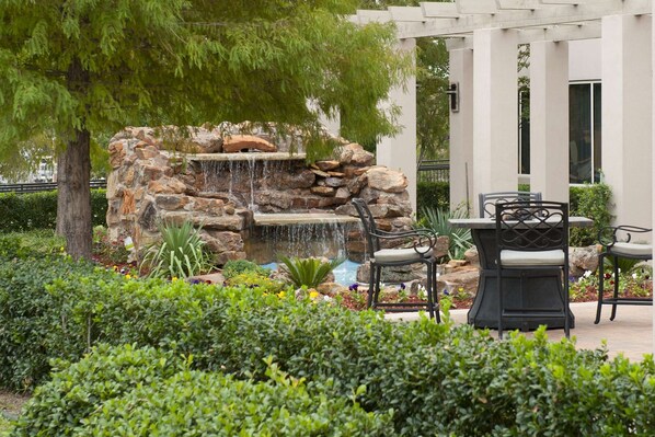 A garden with a stone waterfall, outdoor seating, and a pergola structure.