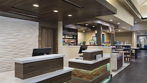 Un espace d’accueil d’hôtel au design moderne, comprenant un comptoir d’accueil, un minibar et un coin salon.