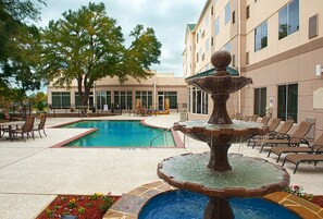 A pool area with a fountain, lounge chairs, and a building with large windows.