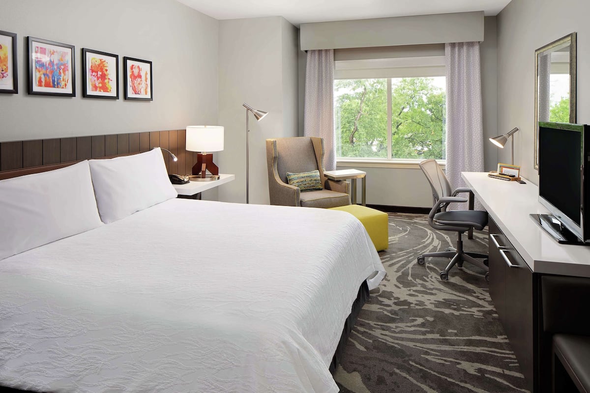 A hotel room with a large bed, a desk with a computer, a chair, and a window with a view of trees.