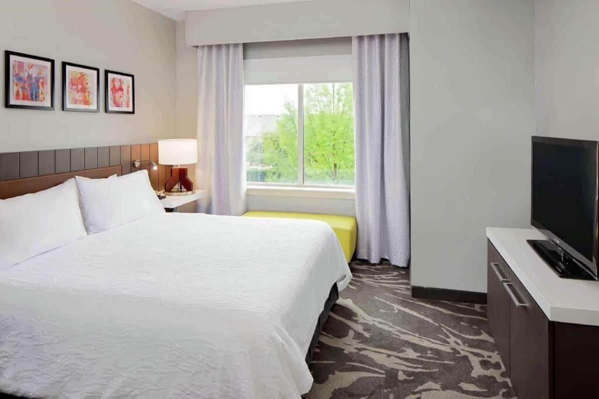 A hotel room with a large bed, a TV, a window with curtains, and artwork on the wall.