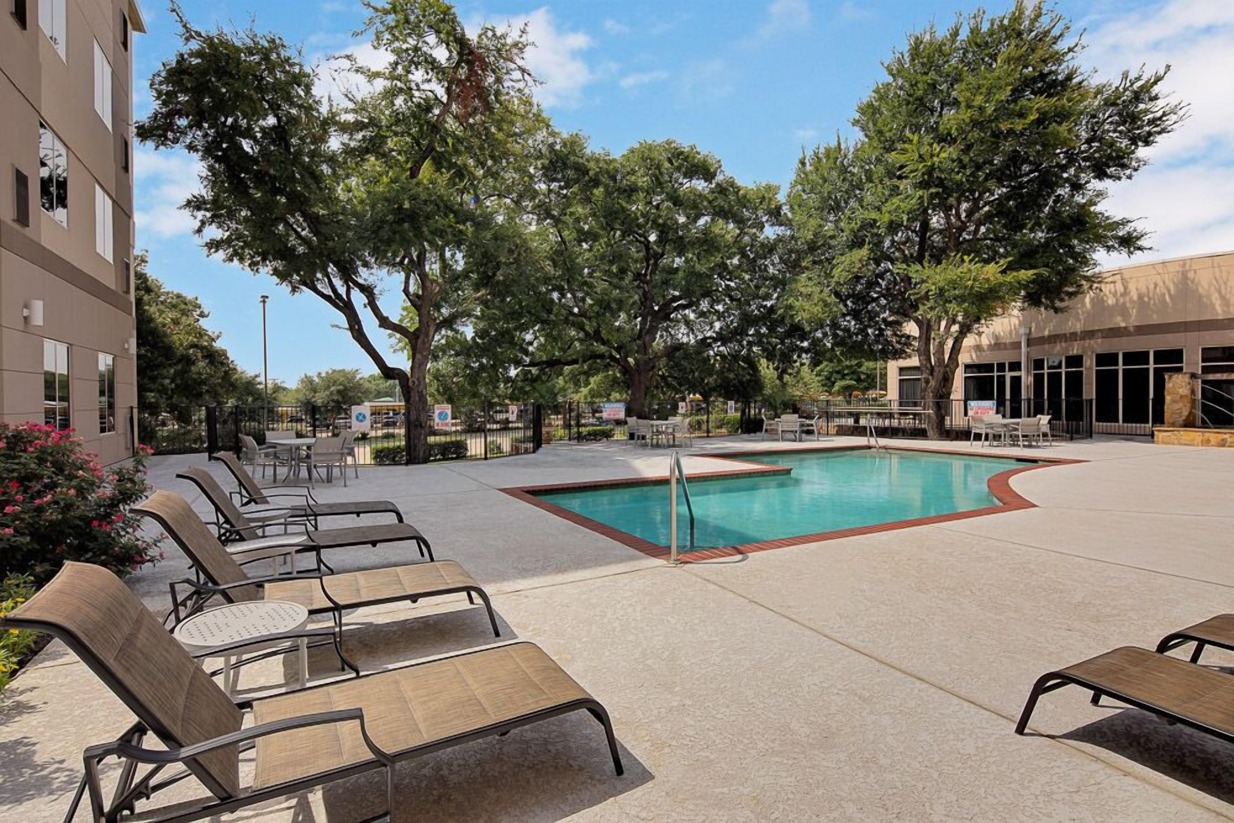 A pool area with lounge chairs, a swimming pool, and surrounding trees.