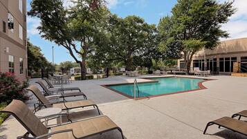 A pool area with lounge chairs, a swimming pool, and surrounding trees.