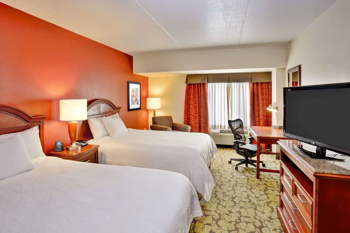 A hotel room with two beds, a desk with a television, and a chair.
